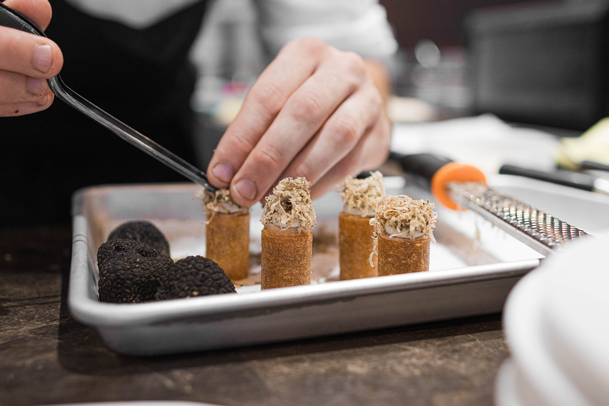 Photo of a chef's hands putting grated truffle on small appetizers.